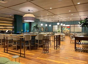 Restaurante com chão de madeira, várias mesas e cadeiras para refeições, luminárias pendentes e parede com padrão azul.