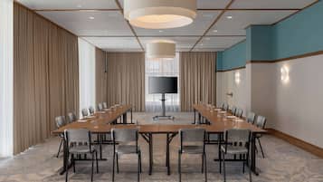 Une salle de conférence avec une longue table, des chaises, un téléviseur à écran plat et un grand luminaire suspendu.