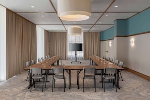 A conference room with a long table, chairs, a flat-screen TV, and a large pendant light.