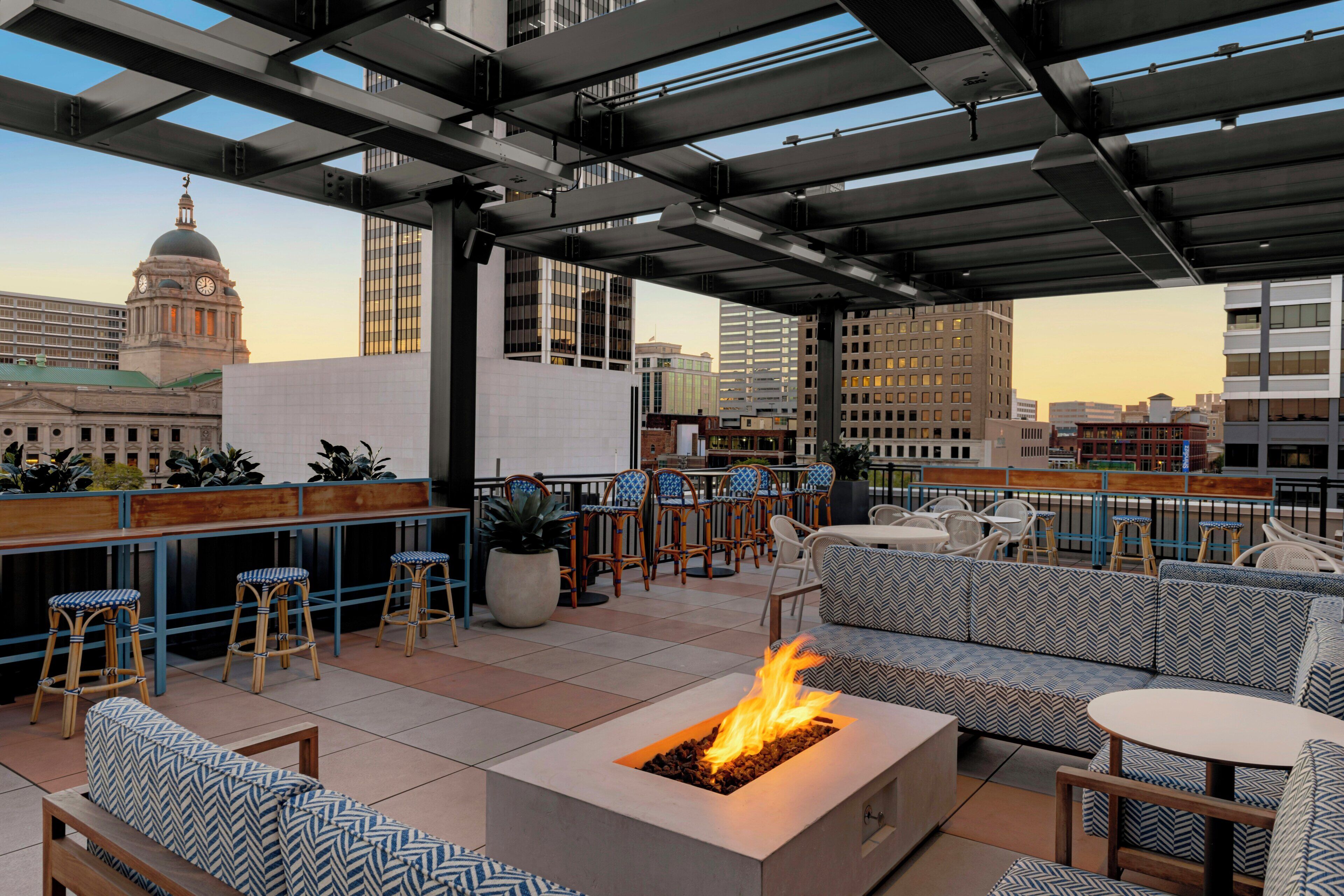 An outdoor seating area with a fire feature, bar stools, and a view of the cityscape.