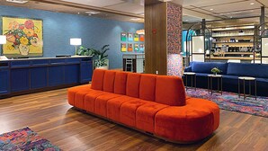 A modern lobby with a wooden reception desk, a vibrant orange sofa, and a blue couch. - The Bradley Hotel (Fort Wayne)