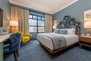 A hotel room with a large bed, a desk, a chair, and a window with curtains. - The Bradley Hotel (Fort Wayne)