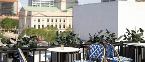 Eine Terrasse mit Korbstühlen und einem Tisch, mit Blick auf eine Stadtlandschaft, deren markantes Gebäude eine Kuppel besitzt.