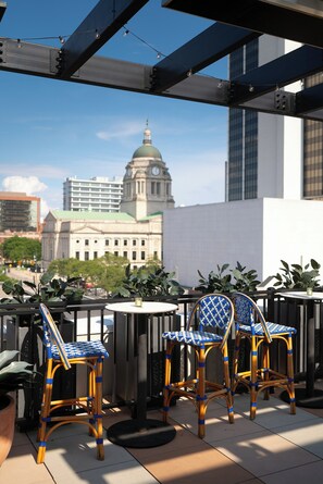 A terrace with wicker chairs and a table, overlooking a cityscape with a prominent building with a dome. - The Bradley Hotel (Fort Wayne)