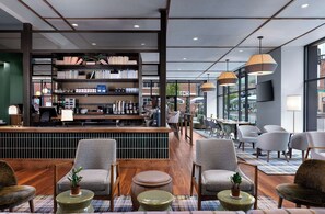 A modern bar area with a bookshelf, seating, and a view of the street. - The Bradley Hotel (Fort Wayne)