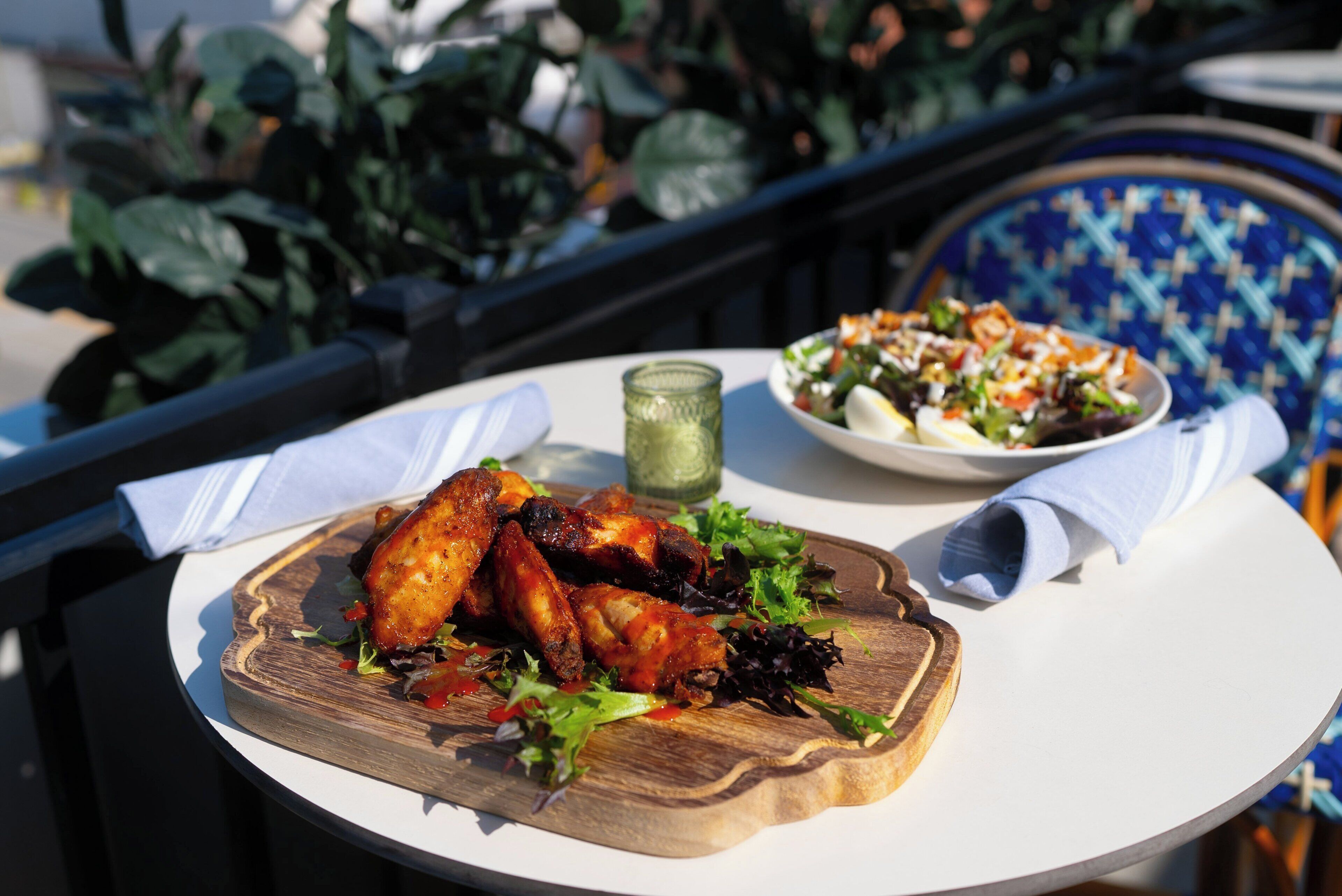 A dining table with a plate of grilled chicken wings and a side salad.