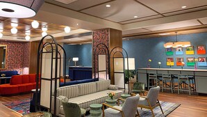 A modern hotel lobby with a sofa, chairs, a dining area, and a large decorative lamp. - The Bradley Hotel (Fort Wayne)