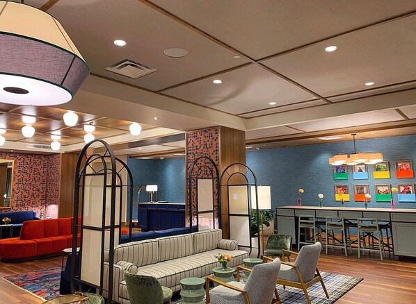 A modern hotel lobby with a sofa, chairs, a dining area, and a large decorative lamp. - The Bradley Hotel (Fort Wayne)