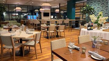 A restaurant with multiple dining tables and chairs, wooden flooring, and pendant lighting.