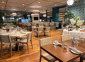 Un restaurante con varias mesas y sillas, suelo de madera e iluminación colgante.