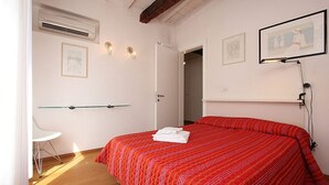 A bedroom with a red bedspread, a white chair, and a door leading to another room. - Appartamento con Terrazze (Venezia)