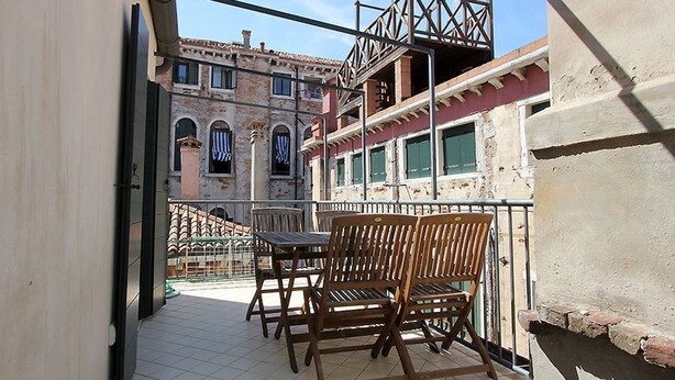 A balcony with wooden chairs and a table, overlooking a historic building with arched windows and a red-tiled roof. - Appartamento con Terrazze (Venezia)