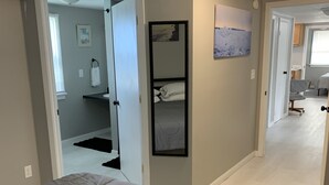Un dormitorio con cama, una puerta que da a un baño y un pasillo con escritorio y silla.