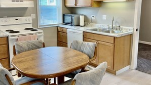 Una cocina moderna con armarios de madera, una estufa blanca, un microondas y un fregadero. Hay una mesa redonda de comedor con cuatro sillas.