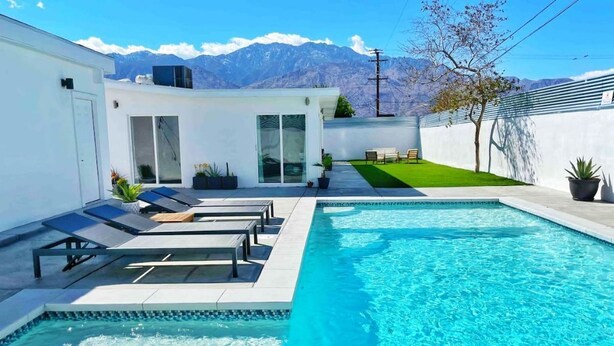 A modern pool area with a clear view of mountains in the background, a small lawn, and a seating area with lounge chairs. - Stylish Palm Springs House with Large Pool (Palm Springs)