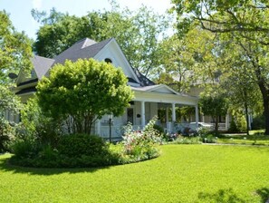 Stunning two-story home with a charming front porch, surrounded by a beautifully manicured lawn and lush greenery.