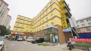 Ett hotell med flera våningar, en gul fasad, en tydligt markerad entré och en parkeringsplats med bilar.