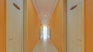 Un long couloir étroit, avec des portes de chaque côté, qui mène à une pièce lumineuse au bout.