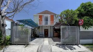 Une maison à deux étages, dotée d’une entrée fermée par un portail, d’un porche abrité et d’un petit jardin devant.