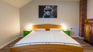 A bed with a wooden headboard, two bedside tables, and a wall-mounted painting of a blue character. - Loftstyle Panorama Bödefeld (Schmallenberg)