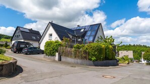A residential area with two houses, one with a sloped roof and solar panels, and a street with parked cars. - Loftstyle Panorama Bödefeld (Schmallenberg)