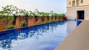 Una piscina con un muro de madera y plantas en un lado, y un edificio con ventanas en el otro.