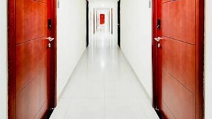 Un pasillo largo y estrecho con puertas rojas a ambos lados y suelo de baldosas blancas.