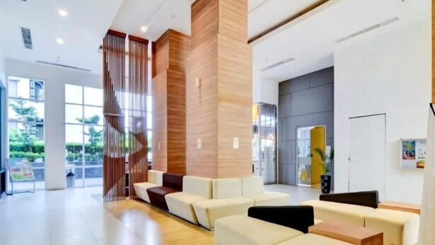 Una moderna zona de recepción con un muro decorativo de madera, un espacio de descanso con sofás y vistas al exterior a través de amplios ventanales.