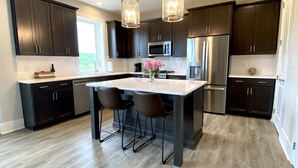 Una cocina moderna con armarios oscuros, electrodomésticos de acero inoxidable y una isla central con taburetes.