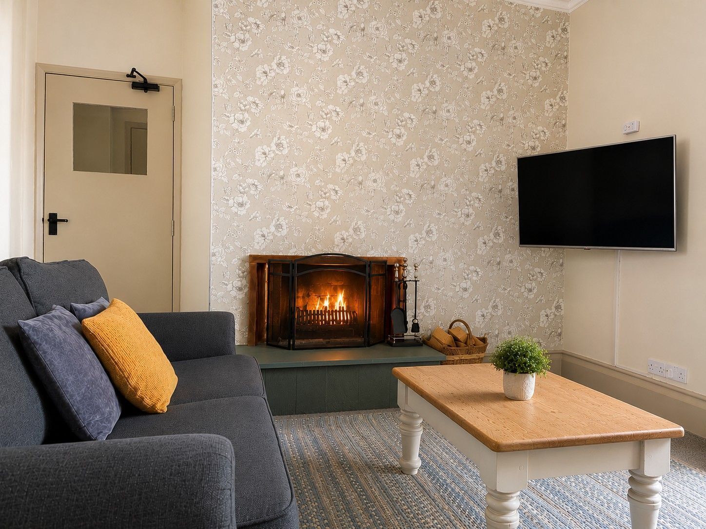 A living room with a sofa, a fireplace, a television, and a small table with a plant.