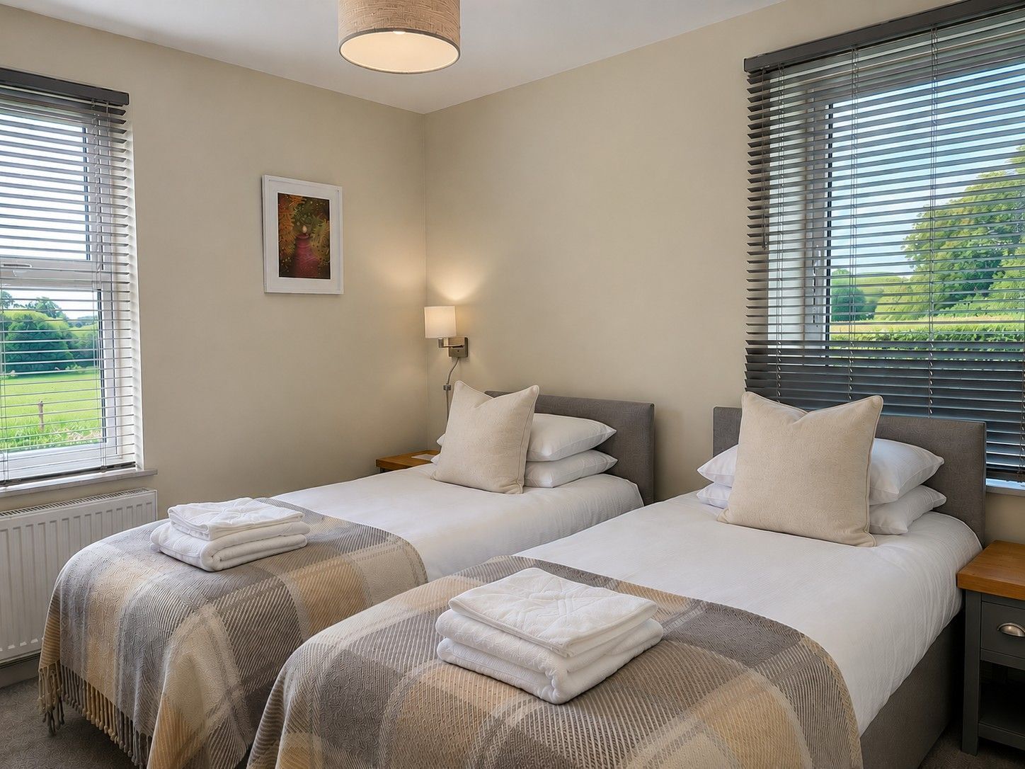 Habitación de hotel con dos camas, una mesita de noche, una lámpara y una ventana con persianas.