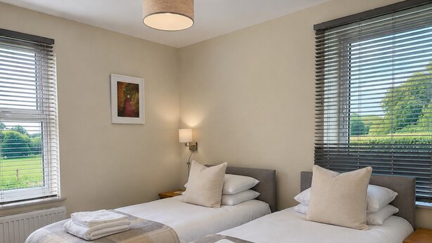 Ein Hotelzimmer mit zwei Betten, einem Nachttisch, einer Lampe und einem Fenster mit Jalousien.