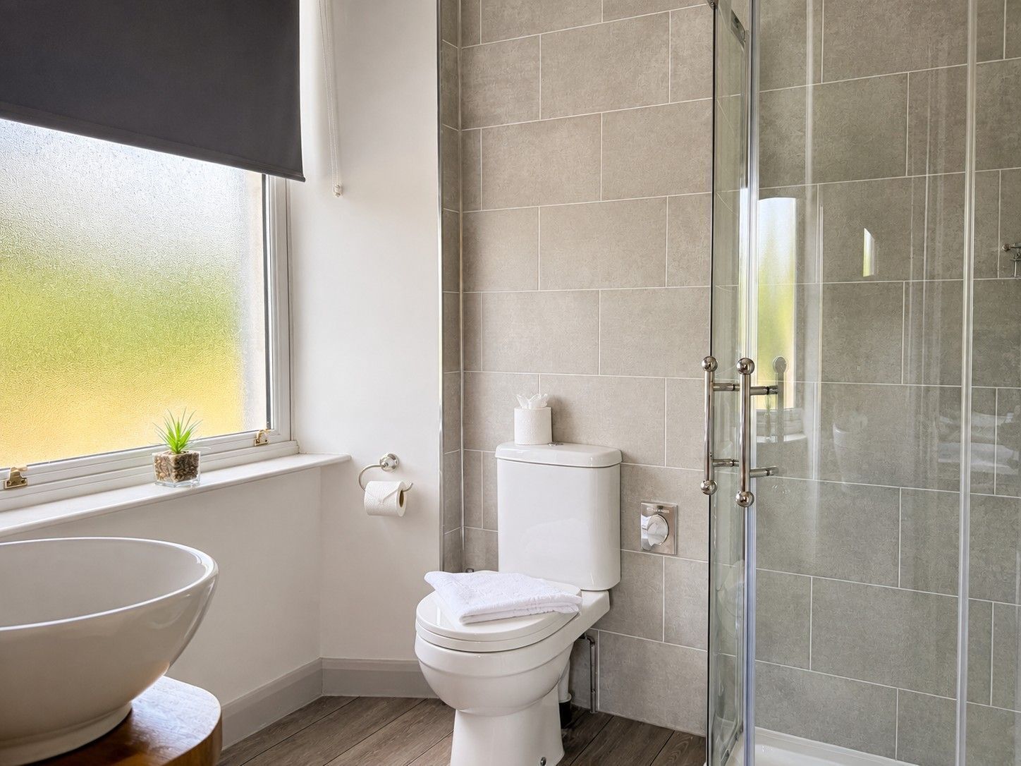 Un baño con inodoro, cabina de ducha de vidrio, lavamanos y ventana con vistas.