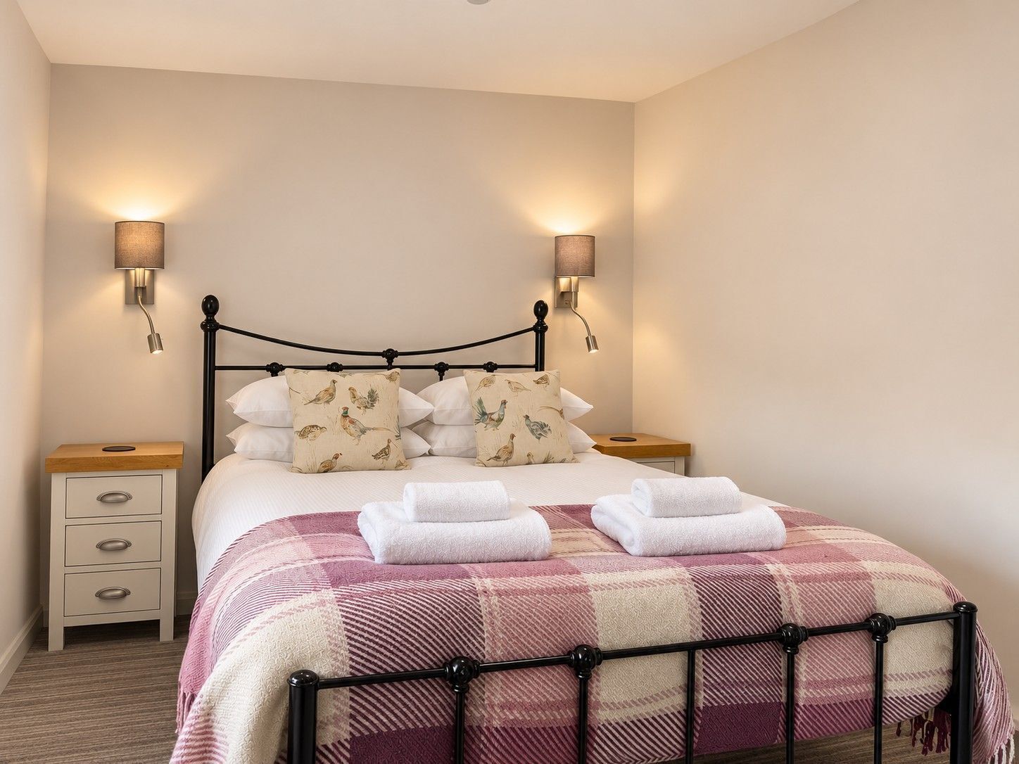 A neatly made bed with a checkered blanket, two wall-mounted lamps, and a bedside table with a drawer.
