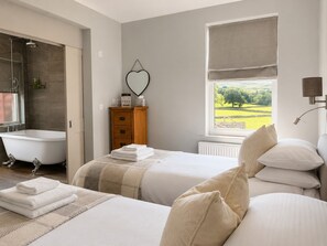 A bedroom with a large window, a bathtub, and a wooden dresser.