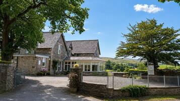 A stone house with a traditional design, a fenced driveway, and a clear view of the surrounding countryside.