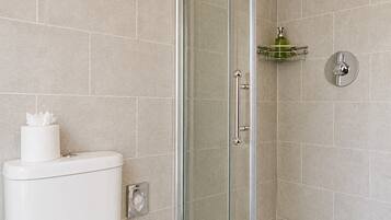 A bathroom with a toilet, a glass shower enclosure, and a green soap dispenser on a shelf.