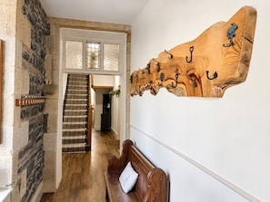 A wooden wall-mounted coat rack with hooks, a wooden bench with a cushion, and a staircase with a striped rug.