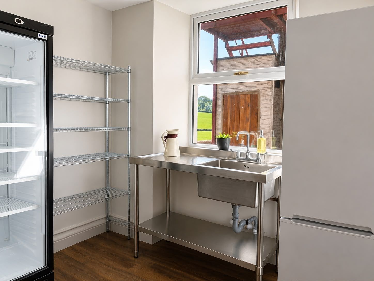 A kitchen with a stainless steel sink, a window with a view of a wooden structure, and a built-in refrigerator.