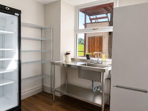 A kitchen with a stainless steel sink, a window with a view of a wooden structure, and a built-in refrigerator.