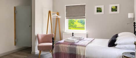Un dormitorio con cama, una silla, ventana con vistas y lámpara colgante.
