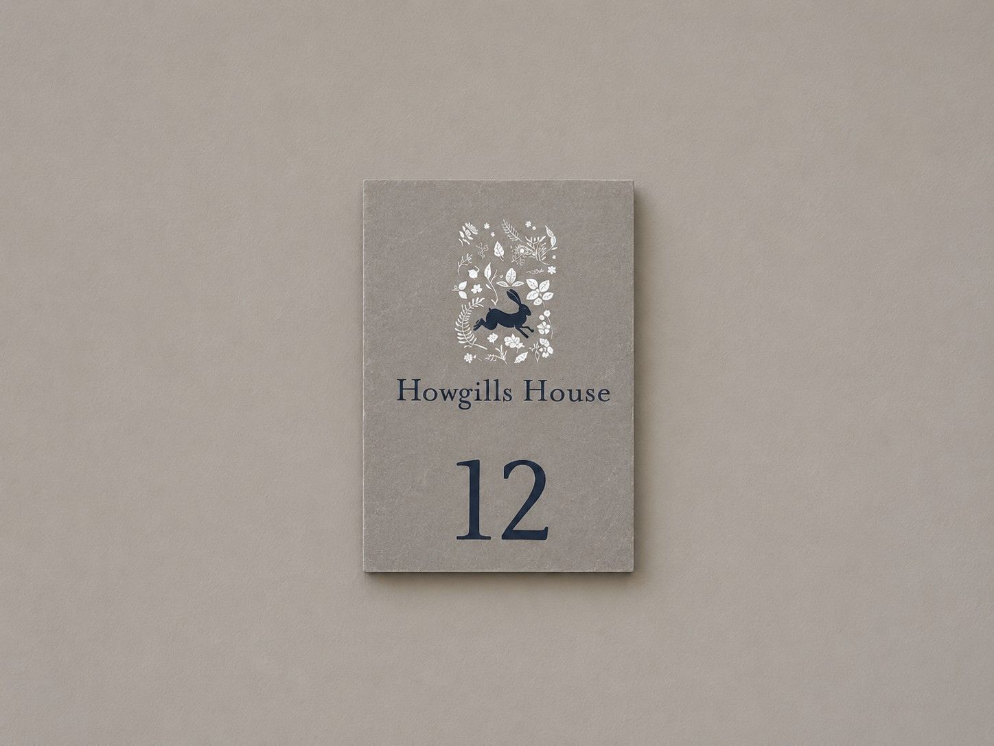 Eine Hausnummer auf einem Schild mit der Aufschrift 'Howgills House' und der Nummer '12' vor schlichtem Hintergrund.