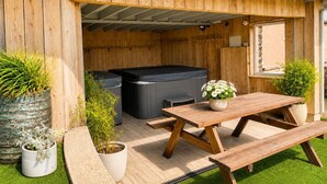 Eine Holzterrasse mit Whirlpool, Tisch und Topfpflanzen.