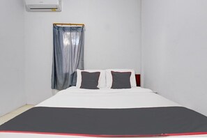 Una habitación pequeña y sencilla con una cama, un ventanal con cortina y un aire acondicionado de pared.