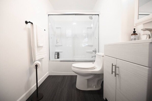 A modern bathroom with a toilet, a glass shower enclosure, a white vanity with drawers, and a towel rack. - ENTIRE APARTMENT RECENTLY RENOVATED 2BR (Ansonia)