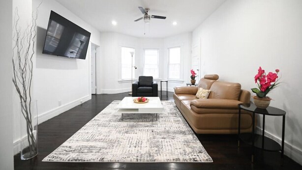 A spacious living room with a large flat-screen TV, a ceiling fan, a brown leather sofa, a coffee table, and a patterned rug. - ENTIRE APARTMENT RECENTLY RENOVATED 2BR (Ansonia)