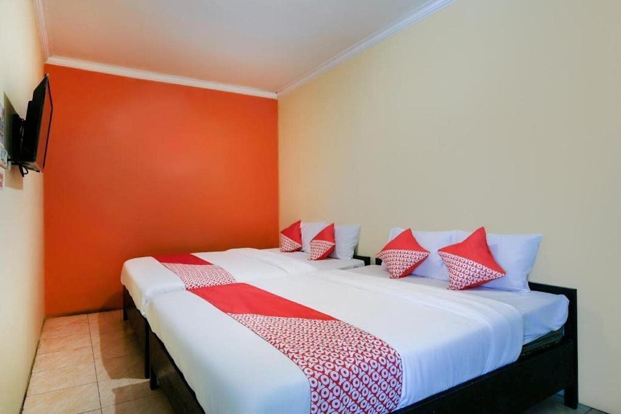 A hotel room with a large bed, orange walls, and a TV mounted on the wall.