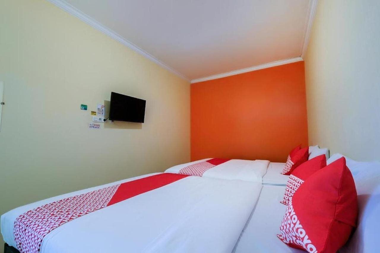 A hotel room with a bed, a television on the wall, and a red and white patterned bedspread.
