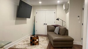 Un salon comprenant un canapé, un téléviseur fixé au mur, une petite table et un vase décoratif.