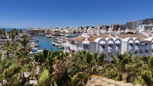Un port de plaisance avec des bateaux, des bâtiments blancs dotés d’arcades et des palmiers.